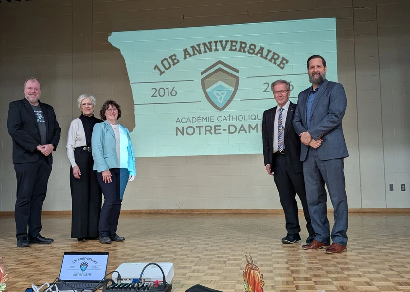 Cinq dignitaires posent sur scène devant une projection soulignant le 10e anniversaire de l’Académie catholique Notre-Dame.