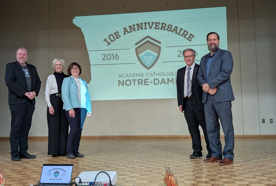 Cinq dignitaires posent sur scène devant une projection soulignant le 10e anniversaire de l’Académie catholique Notre-Dame.